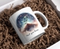Preview: Keramiktasse mit der Illustration einer jungen Pflanze, die unter einem leuchtenden Sternenhimmel wächst, und dem Text 'Plant your dreams', liegend in einer Geschenkbox mit Füllmaterial. Perfekt als inspirierendes Geschenk.